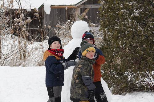 Trois enfants en habits d'hiver construisant joyeusement un bonhomme de neige lors d'une activité hivernale en plein air