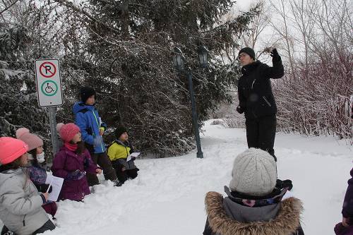 Animateur debout dans la neige présentant une activité éducative à un groupe d'enfants assis en demi-cercle dans un environnement hivernal